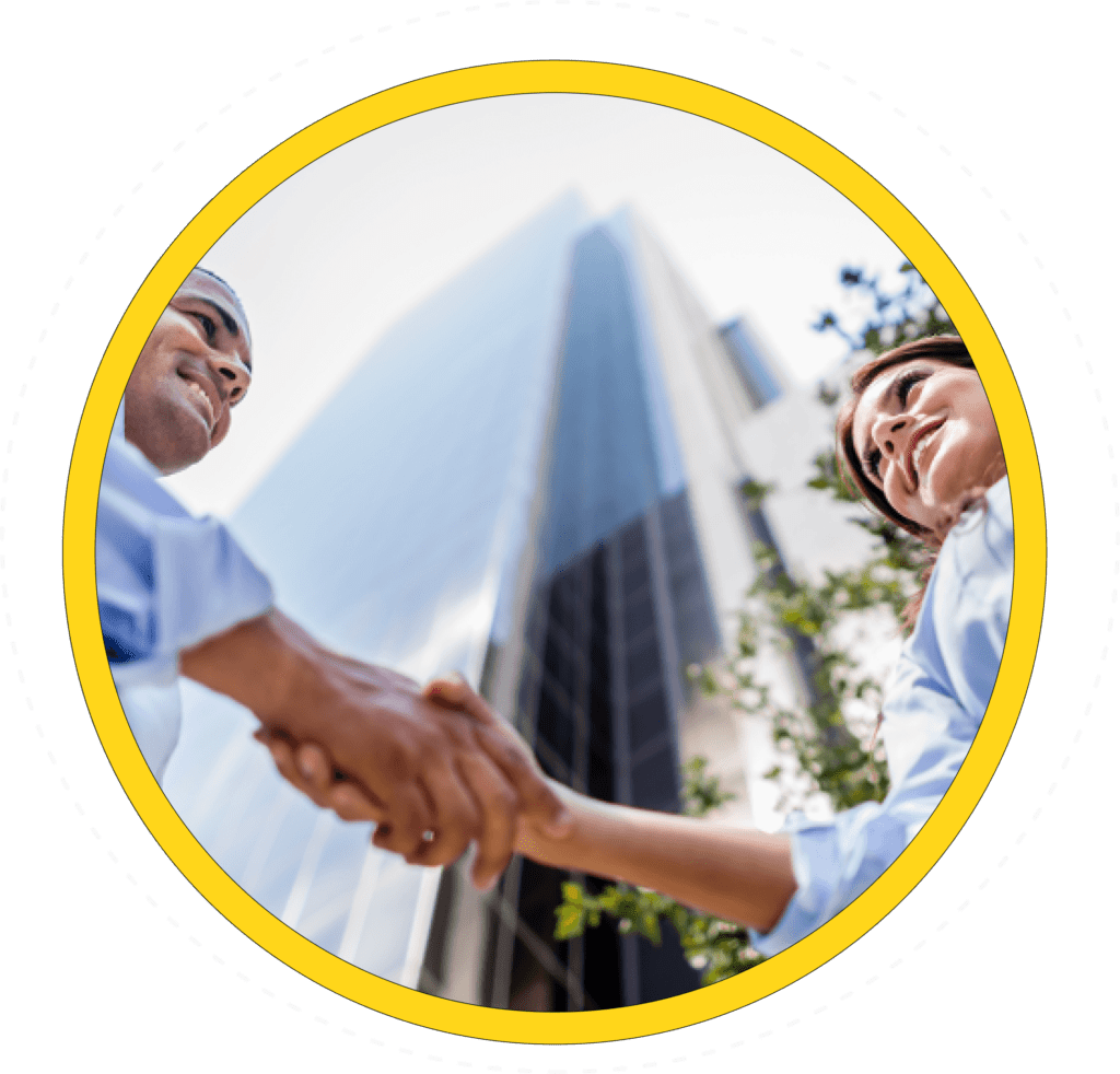 Two businesspeople shaking hands outside a skyscraper, symbolizing partnership.